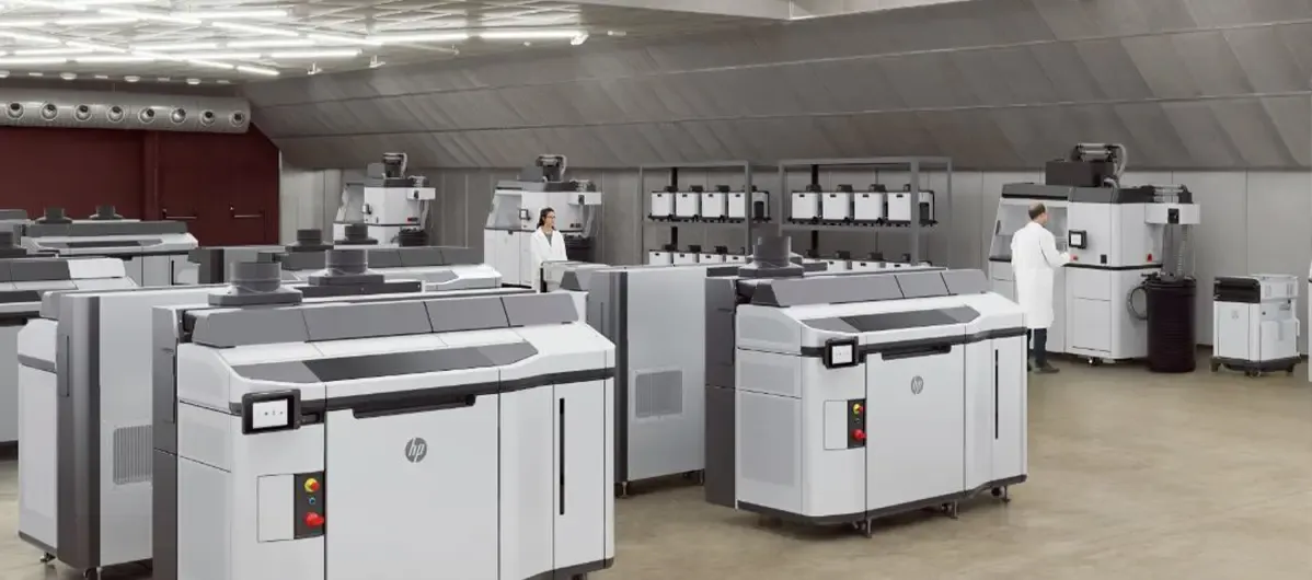 A large production floor lined with rows of white HP 3D printers. Two technicians in white coats are working at machines in the background.