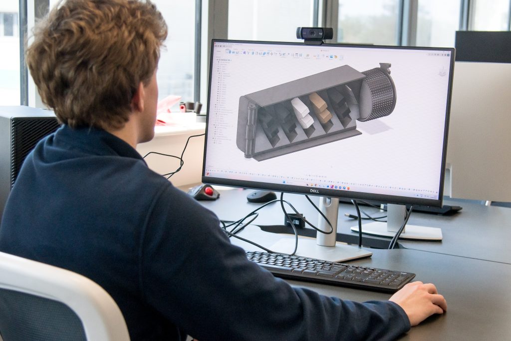 A person sat a computer looking at a fully rendered CGI model of working 3D printed components.