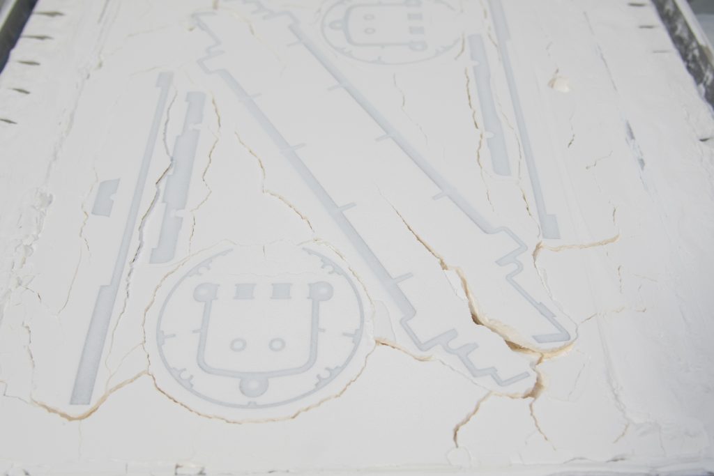 Various 3D printed components sat in a vat of tightly compact white powder ready to be removed.