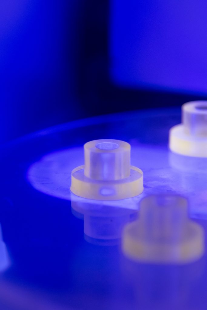 The inside of a 3D printer. The inside is lit by a deep blue light and shows two of six cylinders that sit in the middle of the machine.