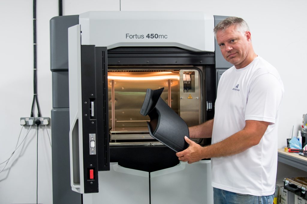 A technician at an industrial FDM printer, holding a printed panel.