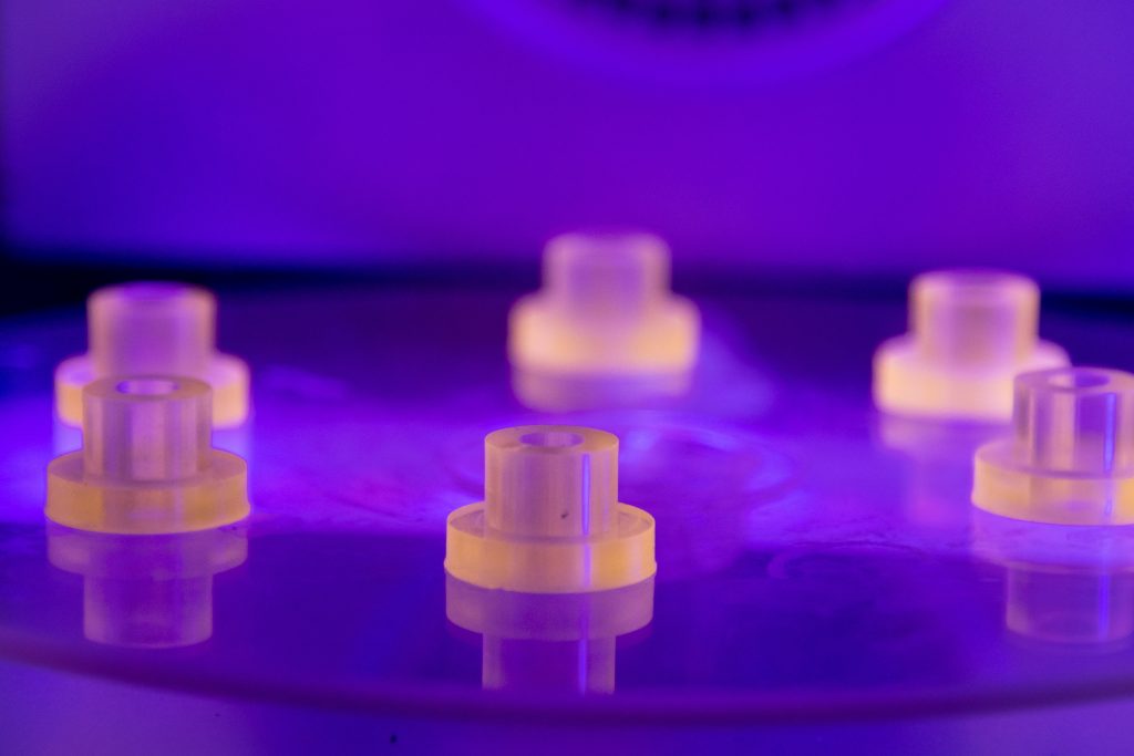 Translucent resin parts on a turntable inside a UV curing chamber, lit purple.