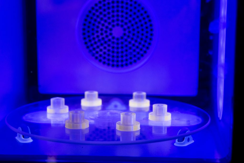Translucent resin parts on a turntable inside a UV curing chamber, lit blue.