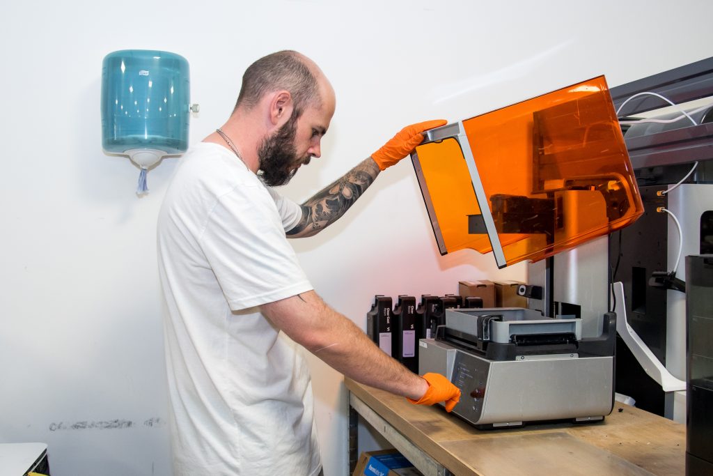 An AMufacture technician opening the amber lid of a resin 3D printer