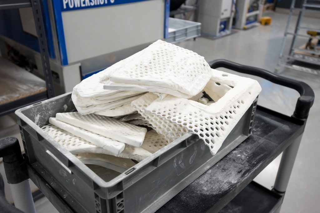 A tray of white nylon lattice parts fresh from an SLS build, stacked on a workshop trolley.