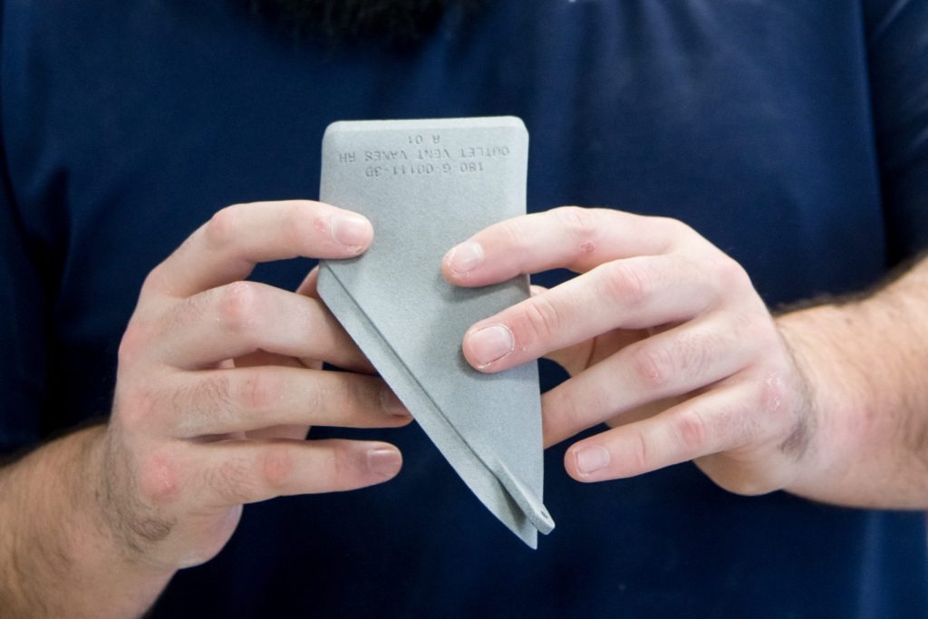 An AMufacture engineer inspecting a 3D printed part, held in both hands.