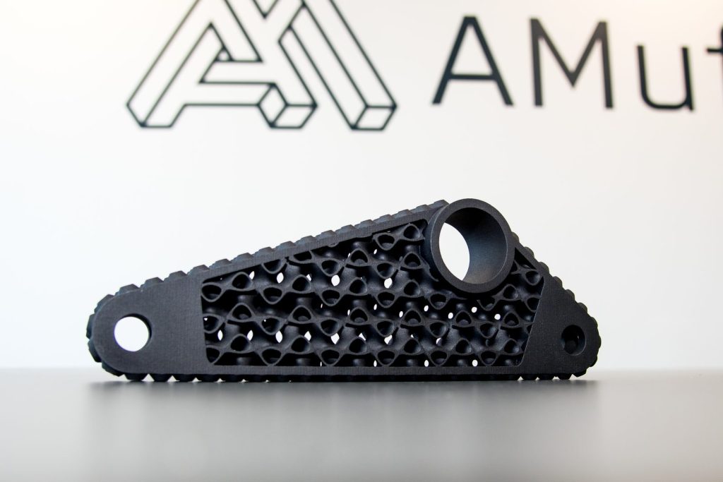 Black 3D printed lightweight arm with an internal lattice structure, in front of the AMufacture logo
