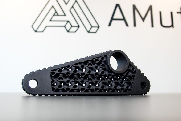 Black 3D printed lightweight arm with an internal lattice structure, in front of the AMufacture logo