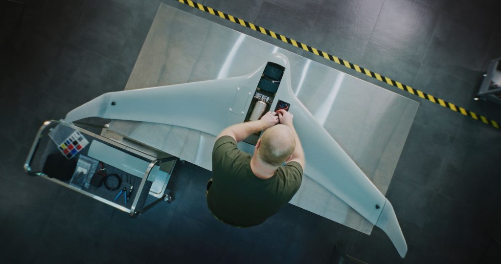 Overhead view of a technician fitting components into the body of a fixed-wing UAV on a workshop bench