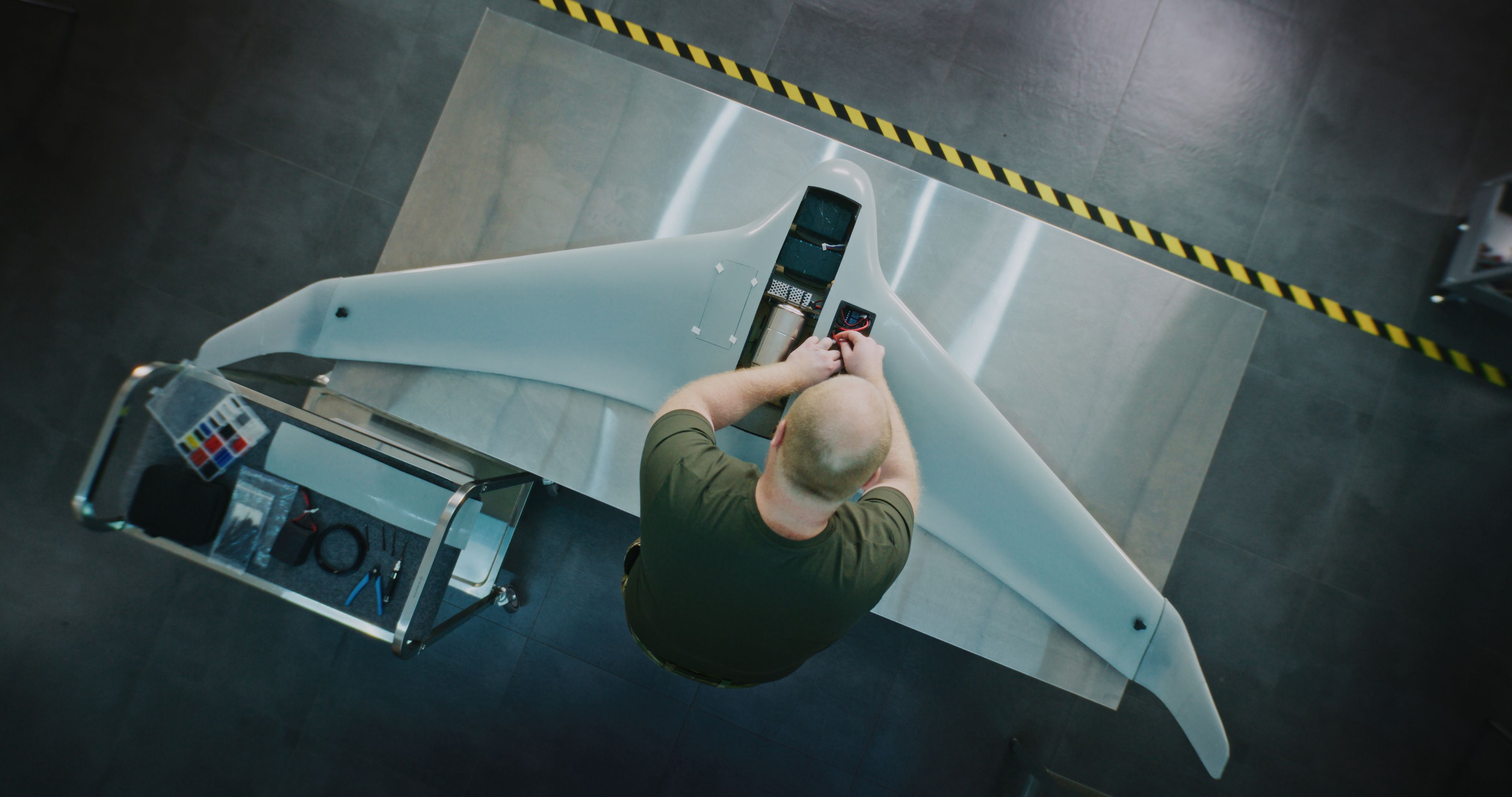 Overhead view of a technician fitting components into the body of a fixed-wing UAV on a workshop bench