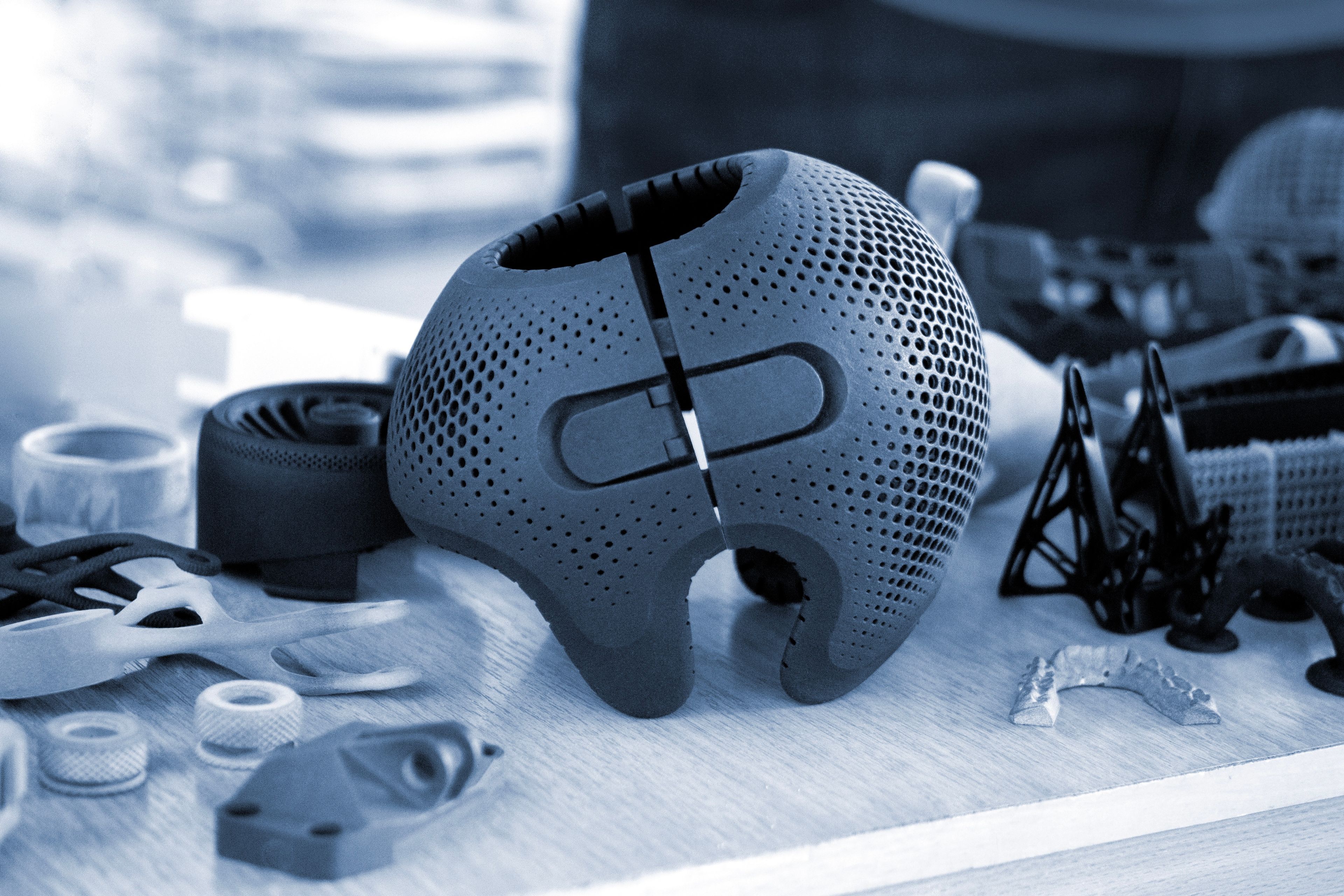A 3D-printed lattice cranial implant on a workbench beside other additively manufactured medical parts