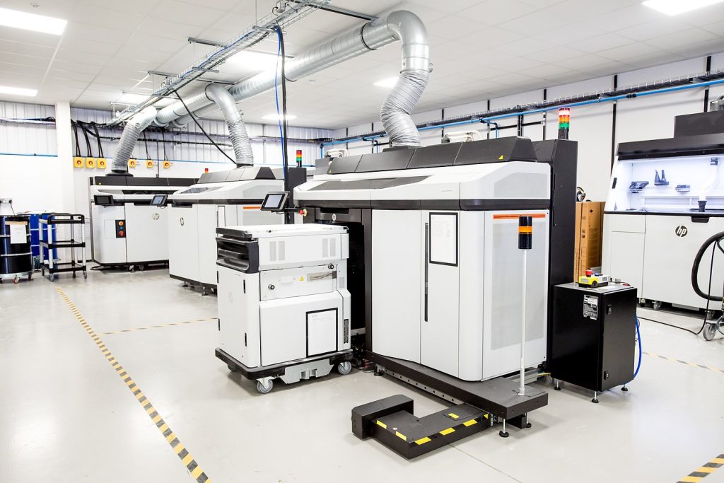 A row of HP Multi Jet Fusion printers on the AMufacture production floor, showing the scale of the fleet.