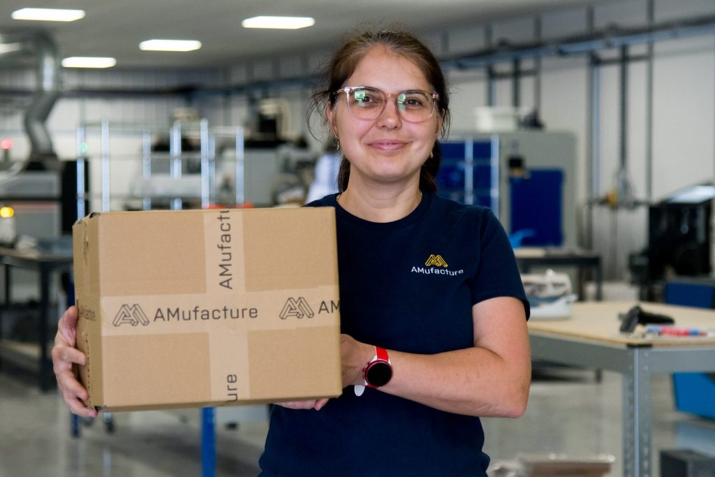 AMufacture team member holding a branded parcel on the production floor