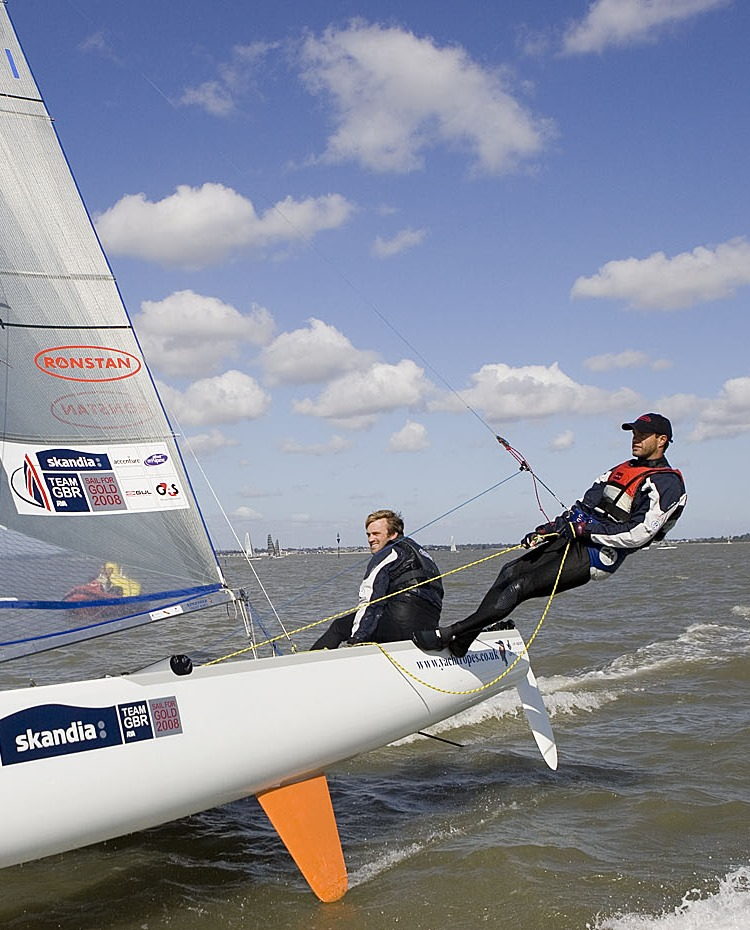 Two crew hiking out on a Skandia Team GBR Tornado catamaran at speed, one on the trapeze.